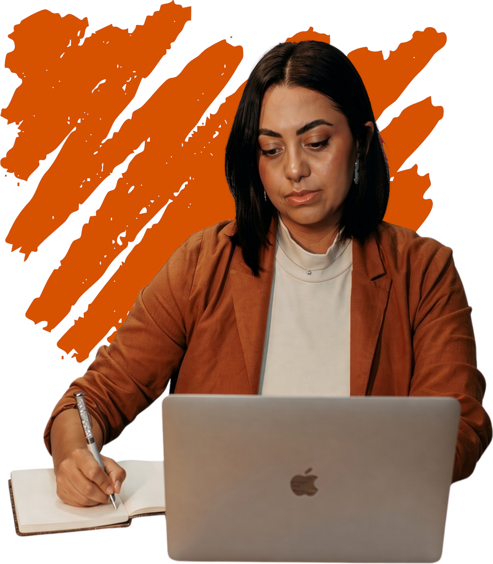 A founder writing in a notebook while working on her laptop